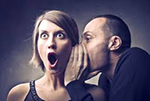 Image of man whispering rumor to woman, who has a shocked look on her face